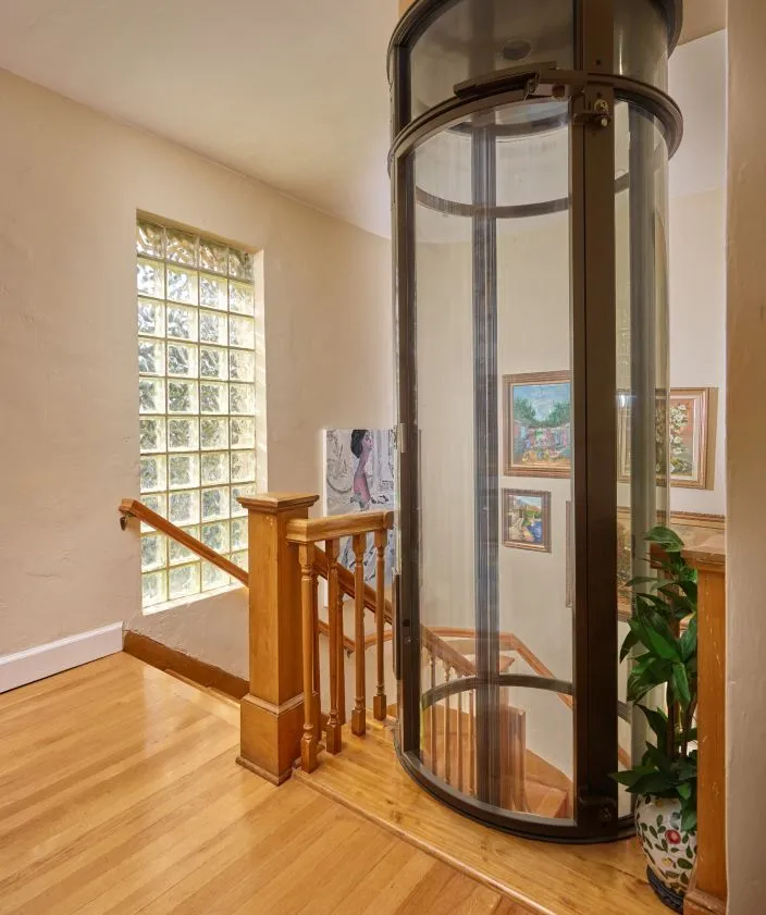 PVE37 round glass home elevator installed beside a wooden staircase for low maintenance residential use