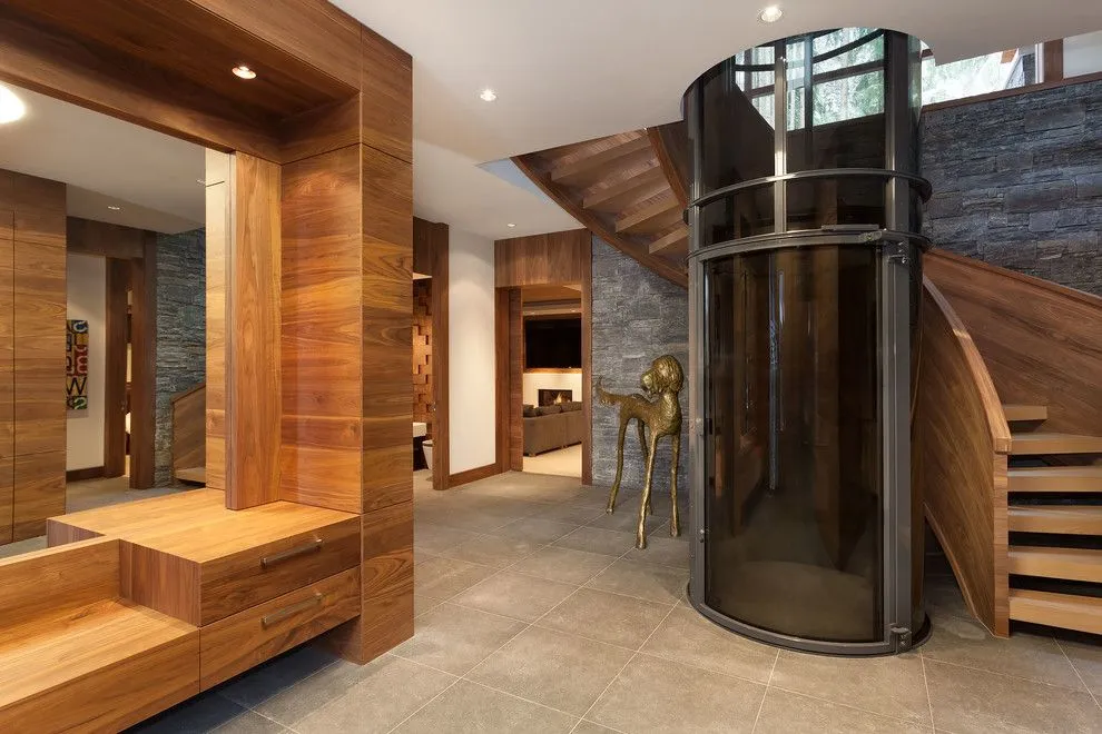 PVE52 pneumatic vacuum elevator with smoked glass tube beside a wooden staircase in a modern home
