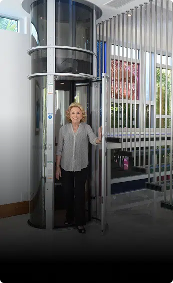 Woman stepping out of a cylindrical PVE home elevator with glass tube and round door