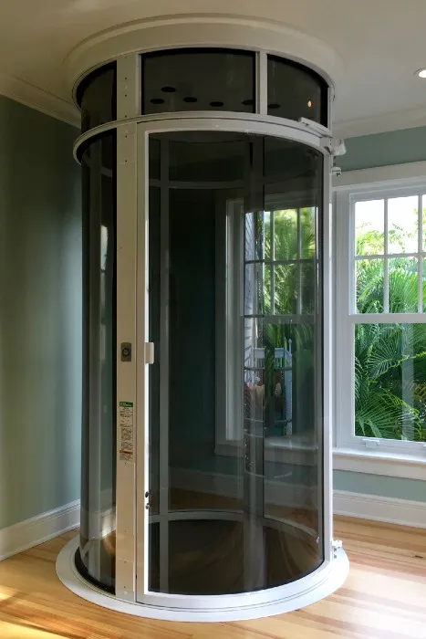 Round pneumatic vacuum elevator with white frame installed in a home corner near a window