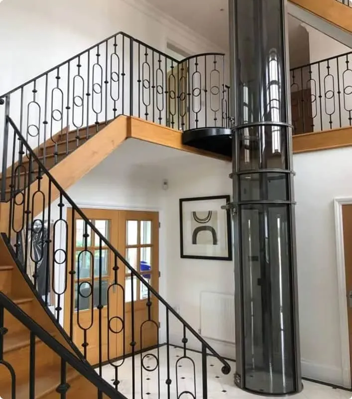PVE30 pneumatic vacuum elevator installed beside a staircase in a two story foyer with wrought iron railings