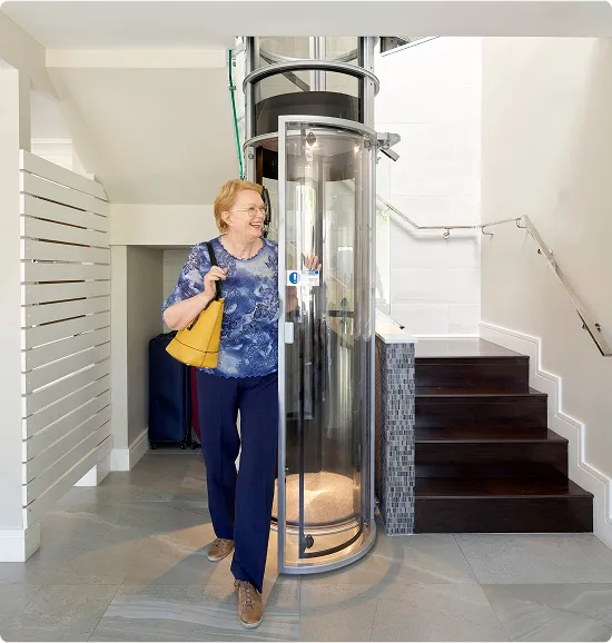 Smiling woman exits the PVE30 round glass home elevator next to a staircase