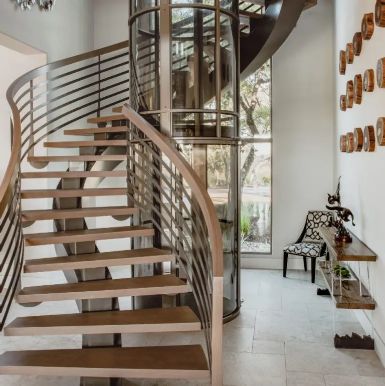 PVE52 pneumatic vacuum elevator with glass cylinder beside a modern floating staircase