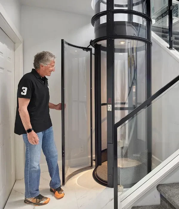 Man opening the curved door of a PVE37 home vacuum elevator next to a staircase