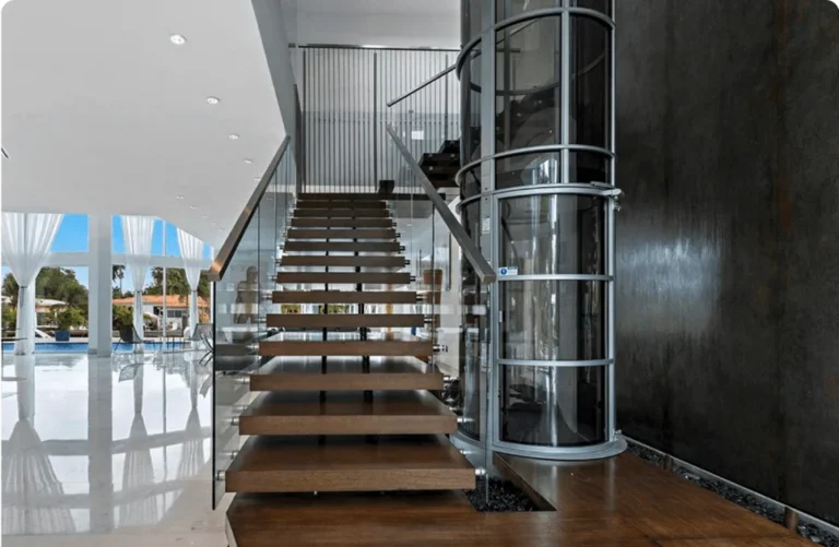Cylindrical PVE home elevator with glass tube beside a modern floating wood staircase