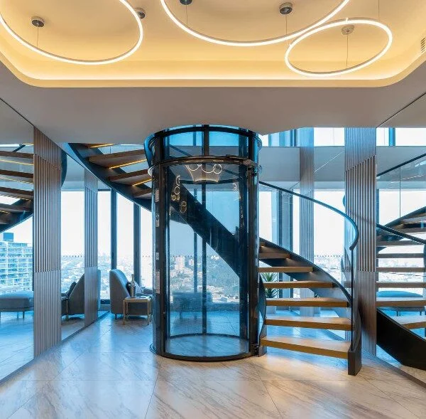 PVE52 round glass vacuum elevator installed beside a spiral staircase in a luxury penthouse