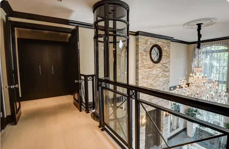 Round glass vacuum elevator installed on a home's upper landing with black trim and stacked stone wall