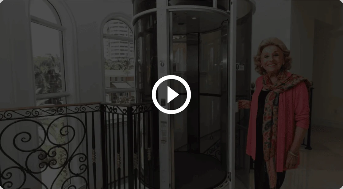 Video play button over a woman standing beside a PVE home elevator with a glass tube
