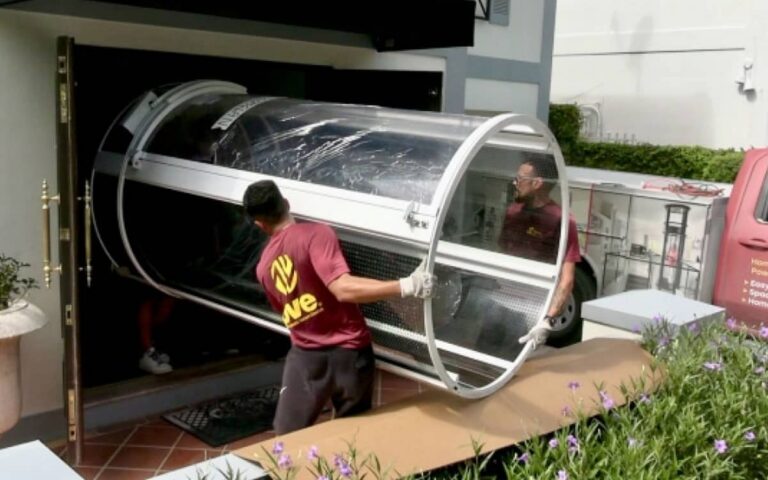 PVE technicians carrying a pneumatic vacuum elevator cylinder into a home for installation