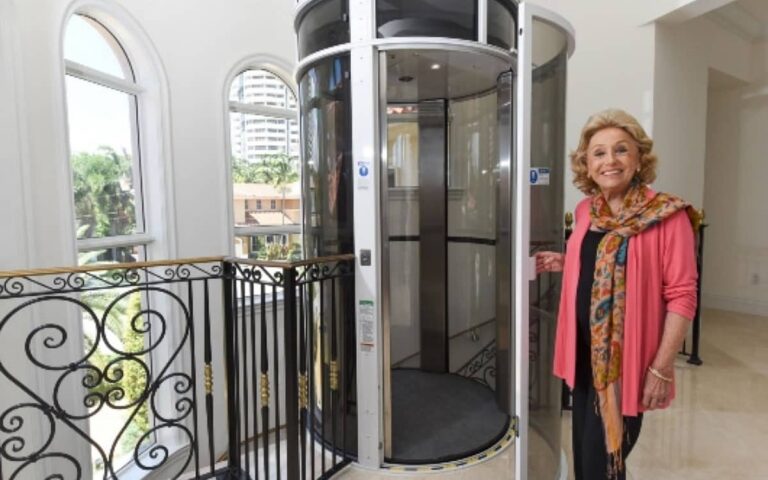 Smiling woman standing beside her installed PVE round glass home elevator on an upper floor landing