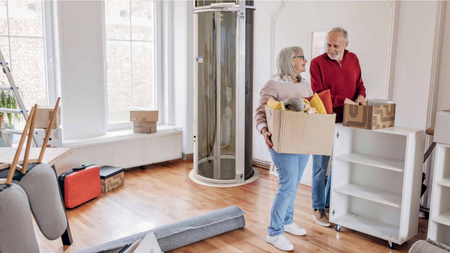 Older couple moving boxes in a new home with a round PVE vacuum elevator installed by the window